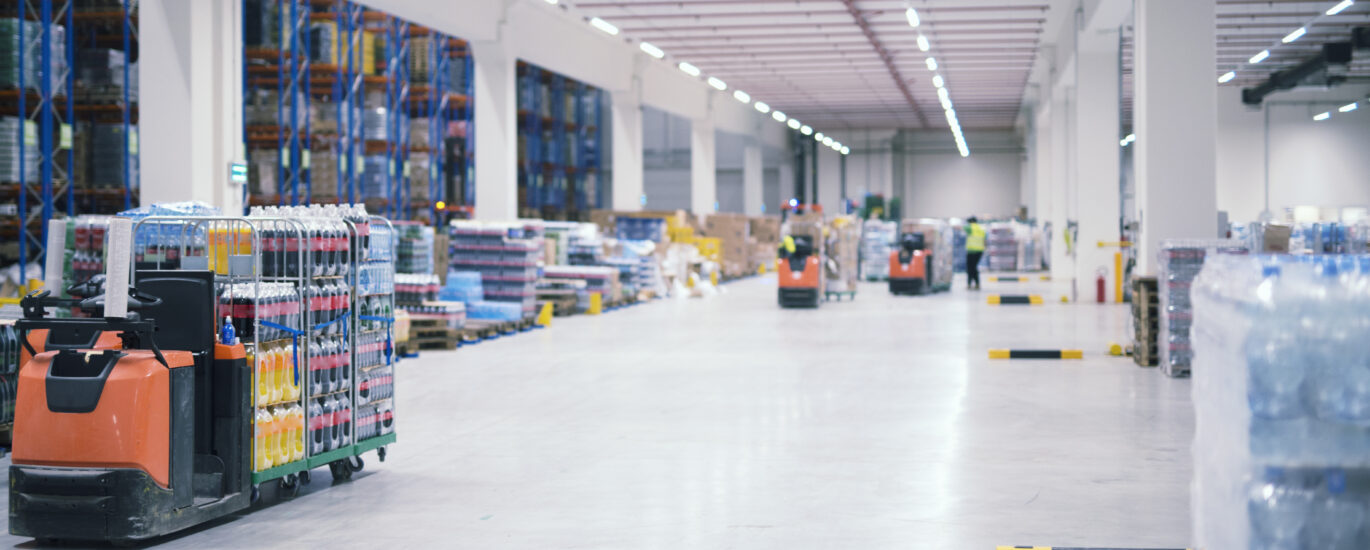 Warehouse industrial building interior with people and forklifts handling goods in storage area.